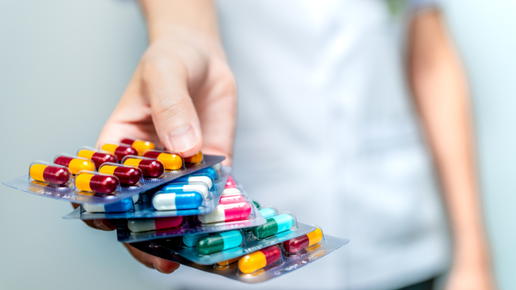 Woman holding 5 blister packs of colorful pills.